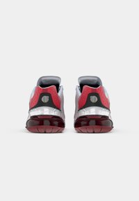 Scarpe atletiche rosse e grigie con parte superiore in rete, collare imbottito, ammortizzazione prominente del tallone e suola in gomma testurizzata. Dettaglio in plastica trasparente.