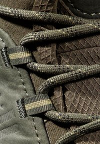 Prim-plan al unei bocanci de drumeție verde măsliniu cu material texturat, găuri țesute și șireturi groase rotunde trecute în mod sigur prin ele.