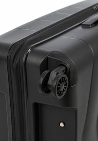 Black hard-shell suitcase featuring a ridged texture, a smooth zipper, and dual black wheels mounted on a durable frame.