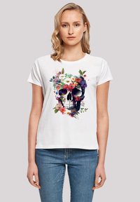 White t-shirt featuring a colorful floral skull graphic, highlighting vibrant flowers in various hues against a dark skull outline.