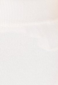 Valkoiset legginsit, joissa on ribbireunus, esittelevät sileää ja venyvää kangasrakennetta. Yksinkertainen muotoilu ilman näkyviä kuvioita tai koristeita.