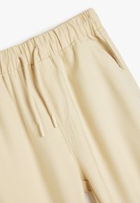 Beige sweatpants med elastisk talje, justerbar snor, sidelommer og en jævn, tekstureret stoffinish.