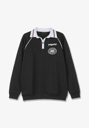 Črna polo jopica z dolgimi rokavi, belim ovratnikom in rdečimi črtami. Ima vezeno logotip s besedilom "KRAJŠI DNEVI, DOLGE NOČI."