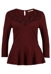 Burgunderfarbene Peplum-Bluse mit langen Ärmeln, die über eine florale Spitze im Schulterbereich und eine Aussparung am Rücken verfügt. Weiches, dehnbares Material für zusätzliche Bequemlichkeit.