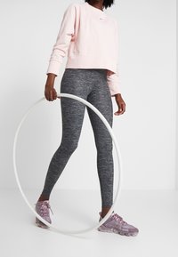 Felpa rosa, leggings grigi con un motivo testurizzato, orecchini a cerchio trasparenti e scarpe da ginnastica viola. Focalizzazione su comfort e design per le prestazioni.