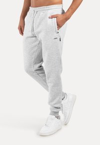 Grå joggers i fleecematerial med konisk design, elastisk midjeband, sidofickor med dragkedja och ribbstickade muddarna, kombinerade med vita sneakers.