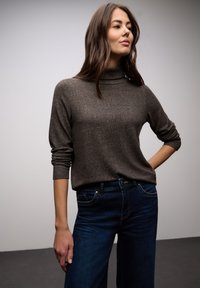 Maglione marrone a collo alto lavorato a maglia con maniche lunghe, abbinato a jeans denim blu scuro con tasche anteriori e vestibilità comoda.