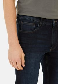Donkerblauwe denimjeans met een rechte snit, met voorzakken en contrasterende oranje stiksels. Soepele textuur en aansluitend ontwerp.