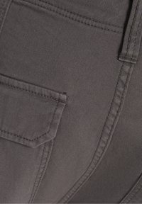 Grå denimtyg som har en synlig söm med detaljer i bakfickan. Texturen är jämn med ett lätt ribbat mönster.