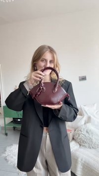 Borsa a mano in pelle color marrone scuro con forma arrotondata, doppi manici corti e dettaglio decorativo a nodo sul lato. Texture liscia.