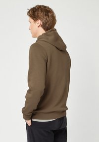 Felpa marrone in cotone con tasca a canguro e polsini a costine, indossata sopra una camicia di tono chiaro. Presenta un cappuccio con cordino e un design senza cuciture nella parte posteriore.
