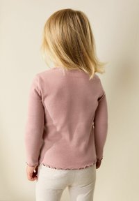 Bluza cu mâneci lungi, cu dungi, de culoare roz pal, cu tiv ondulat, asortată cu pantaloni gri deschis, mulați. Design simplu, minimalist.