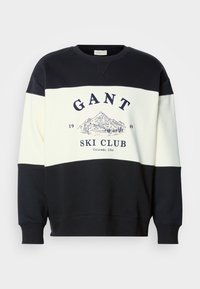 Svetr s barevným blokem v černé a bílé barvě s textem "GANT Ski Club 1949 Colorado, USA" a grafikou hory a lyžaře na hrudi.