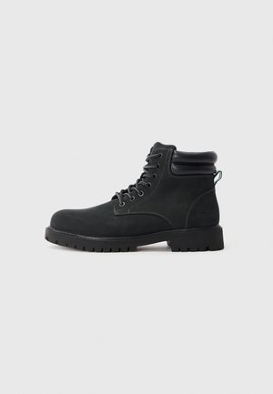 Botas de tobillo de ante negro con suela de goma, puntera redonda y diseño con cordones. Presentan un cuello acolchado y detalles de costura en contraste.