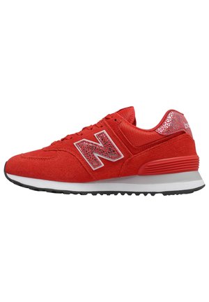 Zapatilla New Balance roja con parte superior de ante y malla, suela blanca y negra, y detalle reflectante con estampado animal en el logo y el talón.