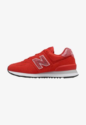 Zapatilla New Balance roja con parte superior de ante y malla, suela blanca y negra, y detalle reflectante con estampado animal en el logo y el talón.