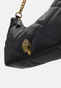 Czarna pikowana torba na ramię z emblematem w kształcie ptaka w złotym kolorze, z łańcuszkowym paskiem i teksturowanym materiałem dla dodatkowego detalu.