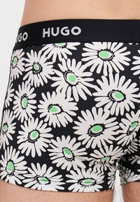 Fekete boxer alsónemű fehér margaréta mintával, zöld akcentussal. A derékpánt fekete, rajta fehér "HUGO" logó.