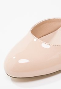 Gros plan sur une ballerine en cuir verni beige brillant avec un bout rond et une doublure intérieure beige.