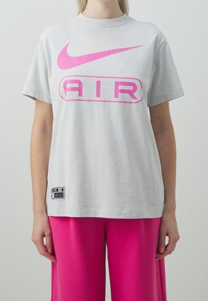 Osoba nosząca jasnoszarą koszulkę Nike Air z dużym różowym logo i jaskraworóżowe spodnie, stojąca na jednolitym tle.