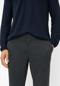 Donkergrijze, gemusterd broek met een subtiel ruitpatroon, voorzien van een knoopsluiting en zijzakken, in combinatie met een marineblauwe overhemd met lange mouwen.