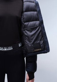 Zwarte pufferjack met een glanzende afwerking, geborduurde textuur en elastische manchetten. Voorzien van een logo patch en een aansluitend zwart topje met een gemerkte tailleband.