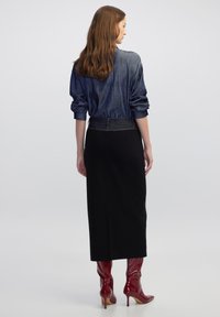 Denim overhemd met opgerolde mouwen, gecombineerd met een zwarte midi-rok. Kenmerkt zich door kniehoge glanzende rode laarzen en een getailleerd ontwerp.