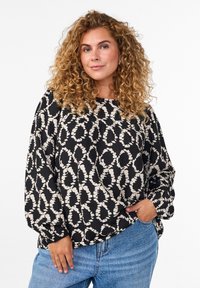 Blouse noire et crème à motifs avec des manches longues légèrement bouffantes et un col arrondi, assortie à un jean en denim taille haute.