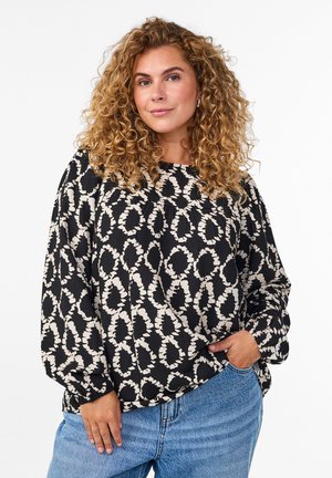 Blouse noire et crème à motifs avec des manches longues légèrement bouffantes et un col arrondi, assortie à un jean en denim taille haute.