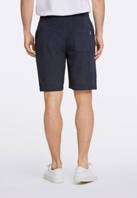 Marina blå bomullsshorts med strukturerad yta, med en bakficka och elastisk midja. Matchas med vita sneakers.