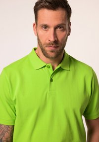 Limetkově zelené bavlněné polo tričko s límečkem, dvěma knoflíky a krátkými rukávy, s hladkou texturou a přiléhavým střihem.