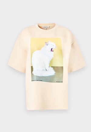 Tricou bej supradimensionat dintr-o țesătură moale, având un grafic mare cu o pisică albă căscând pe un fundal galben și verde, cu text dedesubt.