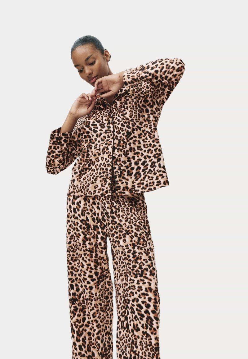 Souprava loungewear s leopardím potiskem vyrobená z měkké látky, obsahující košili na knoflíky a volné kalhoty, s uvolněným střihem a širokými rukávy.