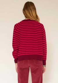 Pull à rayures rouges et roses avec un col arrondi et un ourlet côtelé, associé à un pantalon en velours côtelé assorti. Texture douce, coupe décontractée.