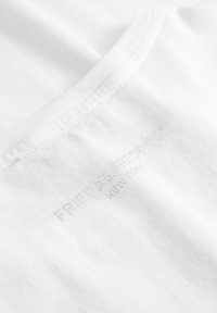 Witte katoenen T-shirt met een gladde textuur en een ronde hals. Kenmerkt zich door subtiele reliëfbranding "FRIEDA & FREDDIES® NEW YORK" nabij de zoom.