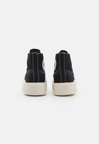 Czarne sneakersy typu high-top wykonane z materiału płóciennego z białymi szwami i gumową podeszwą. Posiadają okrągłą naszywkę z logo na zewnętrznej części kostki.