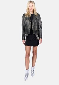 Zwart leren motorjack met een cropped ontwerp, zilveren details, lange mouwen en een riem in de taille, gecombineerd met een zwarte jurk en zilveren enkellaarsjes.