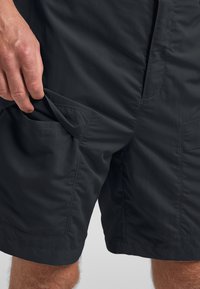 Pantaloni corti leggeri di colore grigio scuro con una texture liscia, dotati di tasche laterali e cuciture rinforzate. Progettati per comfort e mobilità.