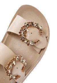Beige slide sandal with two wide straps and circular, embellished buckles featuring clear and gold-toned crystals. Smooth texture.