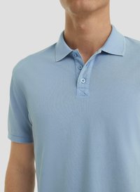 Homme portant un polo à manches courtes bleu clair avec un col et trois boutons, sur un fond blanc uni.