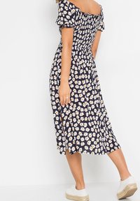 Námořnické květinové šaty s nabíranými rukávy, žlutým a bílým vzorem pampelišek, smockovaným tělem a středně dlouhou volnou sukní s bočním rozparkem.