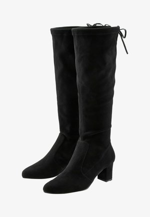 Black suede knee-high boots feature a block heel and side cutouts. The upper has a smooth texture with a tied accent at the top.