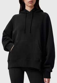 Svart oversized hoodie i mjukt material. Har en justerbar huva, framficka och ribbade ärmslut samt nederkant. Slät yta.