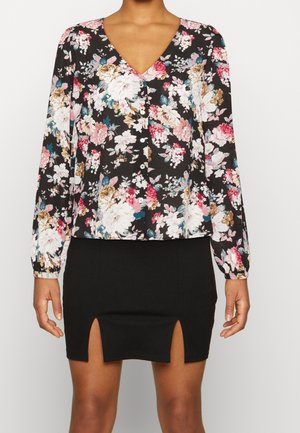 Blusa floreale a maniche lunghe con scollatura a V, caratterizzata da fiori rosa, bianchi e blu su uno sfondo nero; abbinata a una mini gonna nera con fessure.
