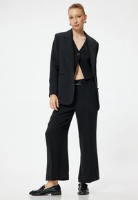 Svart skräddarsydd kostym med en knapp på jackan, kort topp och vida byxor. Texturerade svarta skor fulländar outfiten.