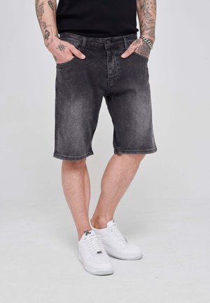 Black denim shorts with a faded texture, straight cut, and visible stitching details. Paired with white sneakers.