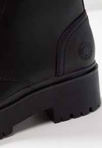 Botas de cuero negro con una superficie texturizada, suela de goma gruesa con estrías y un detalle de logo circular en el talón.