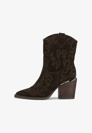 Bottine de cowboy en suede marron avec un bout pointu, motif brodé en tourbillon, et un talon en bois avec un accent argenté. Design élevé et angulaire.