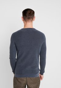 Maglione a coste navy con maniche lunghe e scollatura rotonda, caratterizzato da una texture liscia e un design aderente, mostrato da dietro.