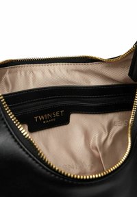 Interno di borsa in pelle nera con rivestimento beige, zip dorata e etichetta con logo. Presenta una tasca con cerniera per l'organizzazione.